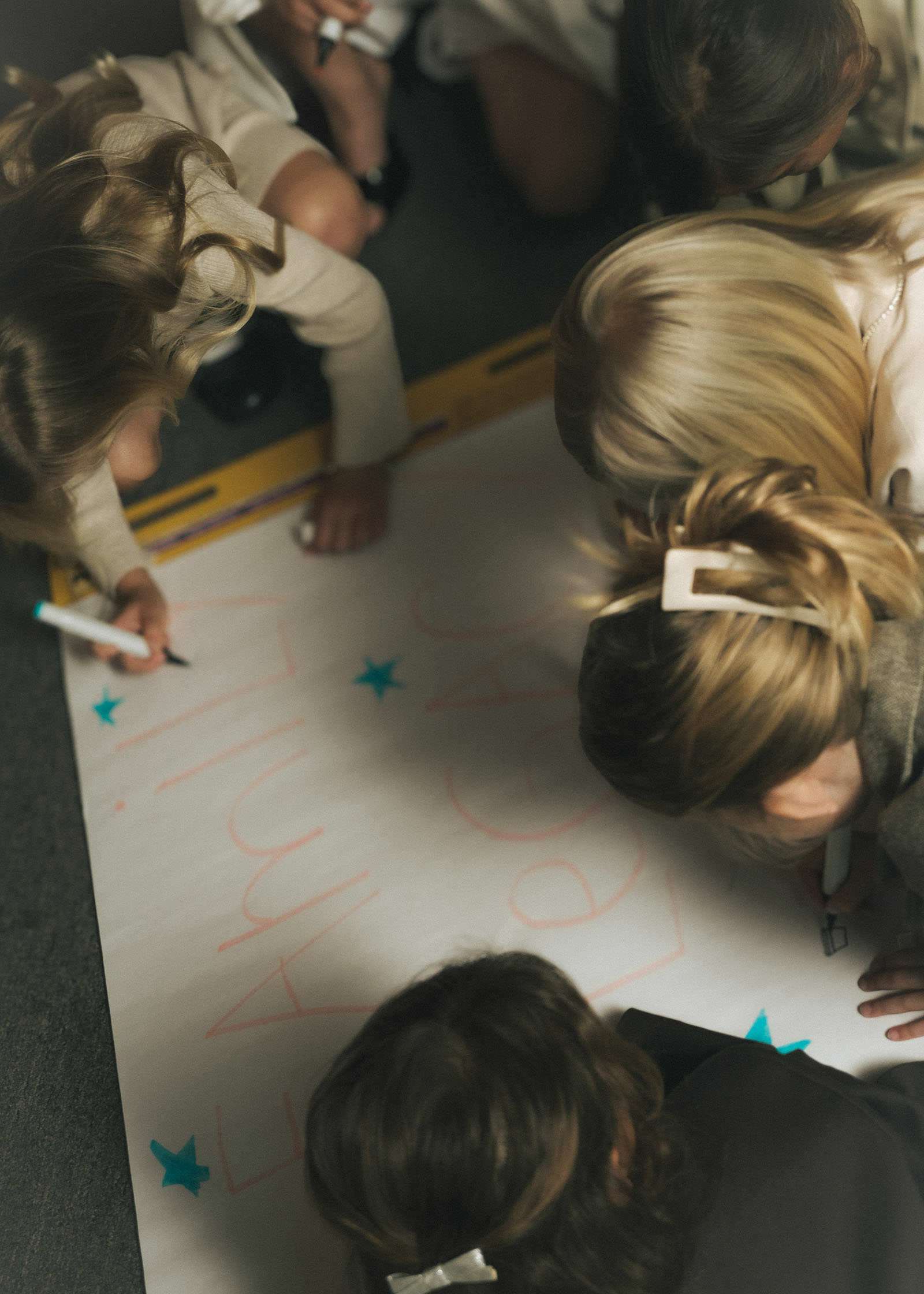 A group of girls writing out "Family Legacy" and decorating a large poster with markers on the floor