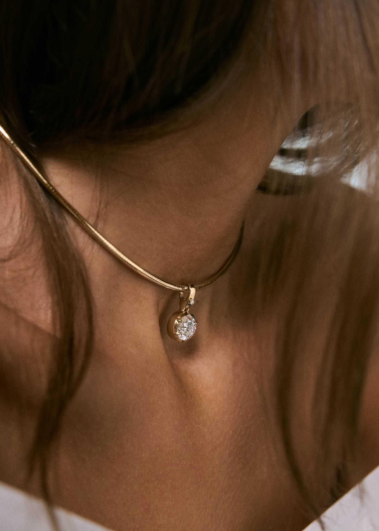 A close up of a woman wearing a Kinn 14k gold Madeleine 2.5ct Round Diamond Pendant on an Heirloom Curved Chain Necklace