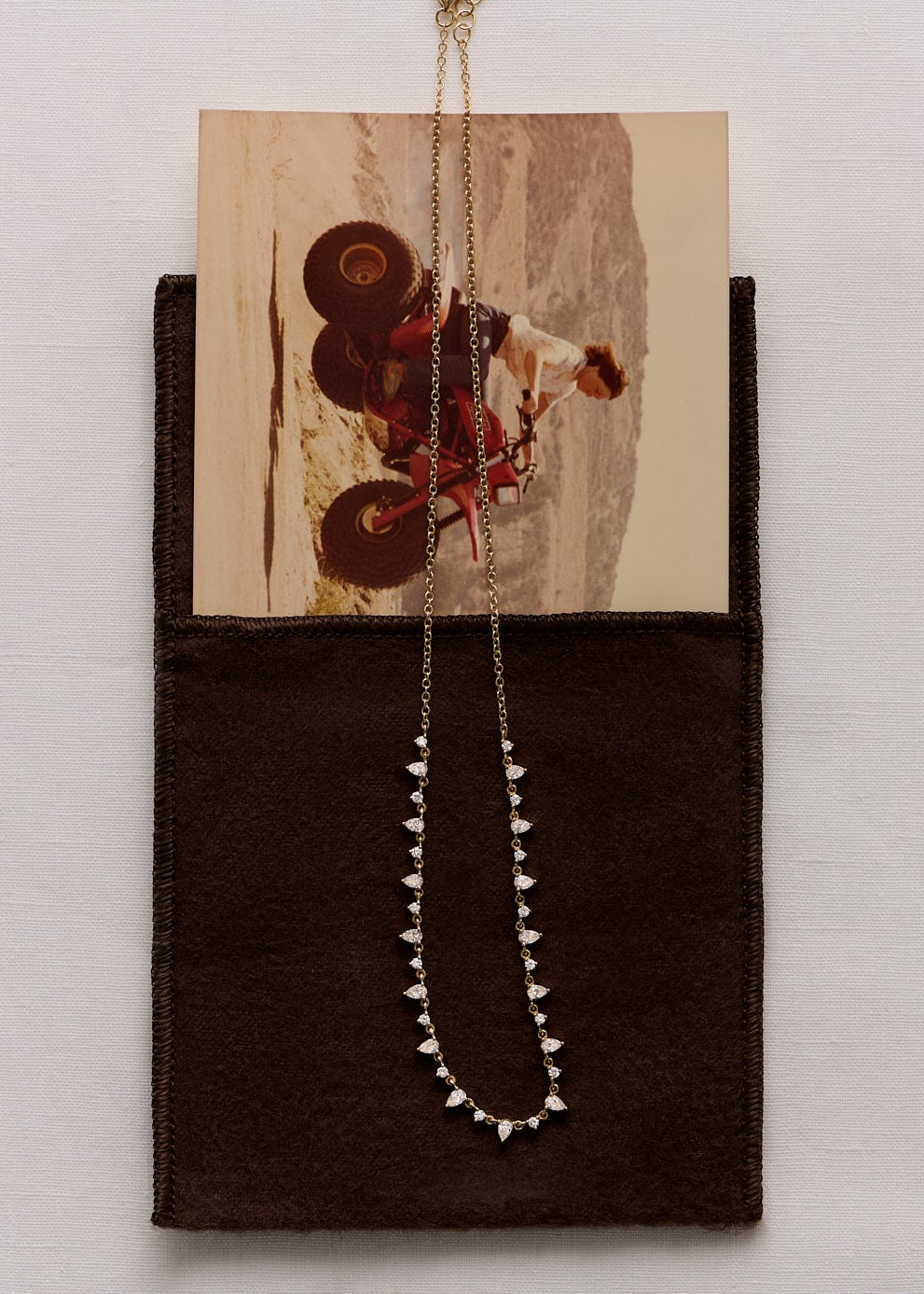 a Kinn 14k Gold Juliette Diamond Row Necklace laying across a photo tucked into a cloth pouch