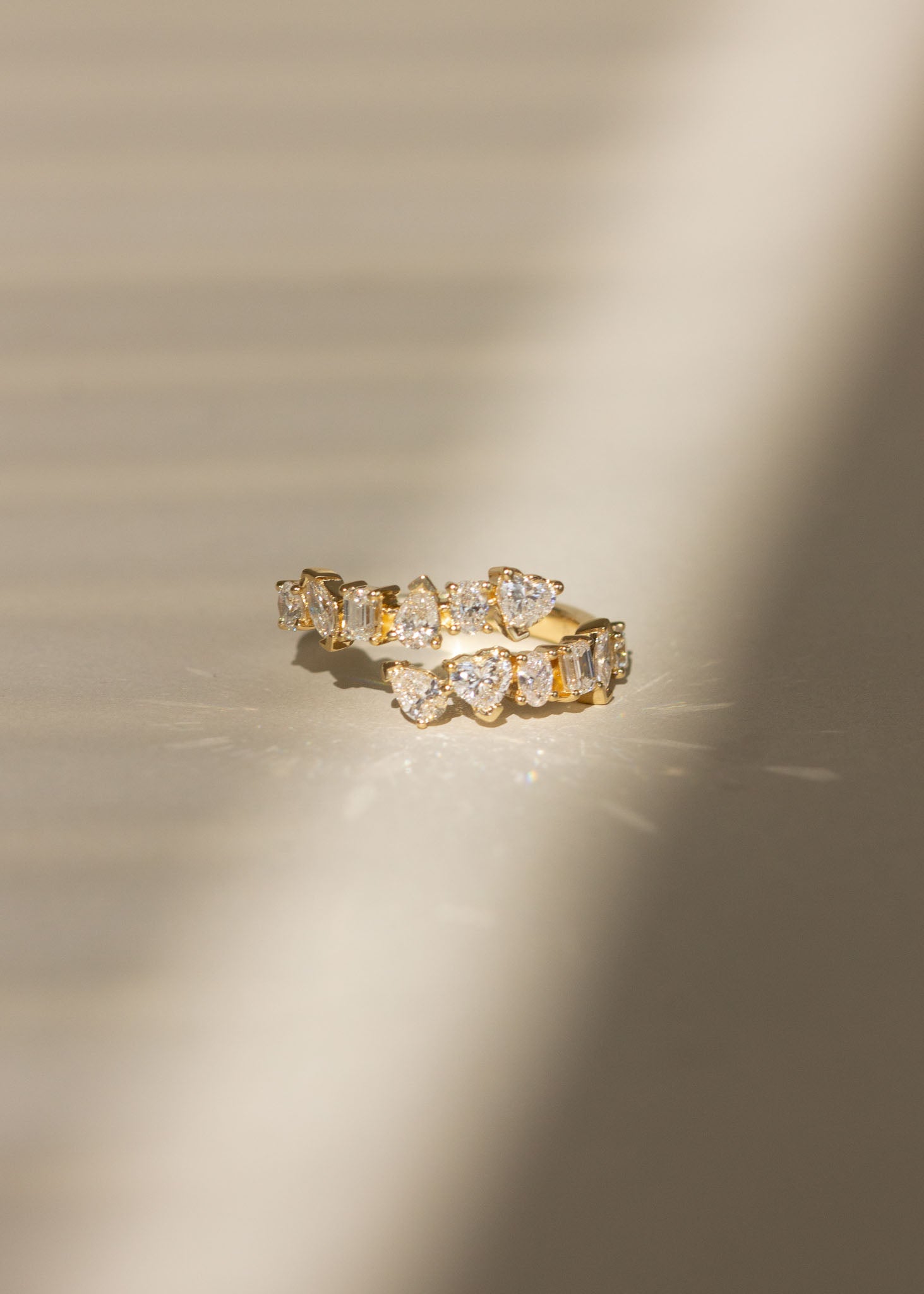 A Kinn 14k Gold Aria Fancy Cut Diamond Wrap Around Ring laying flat and sparkling against a ray of light