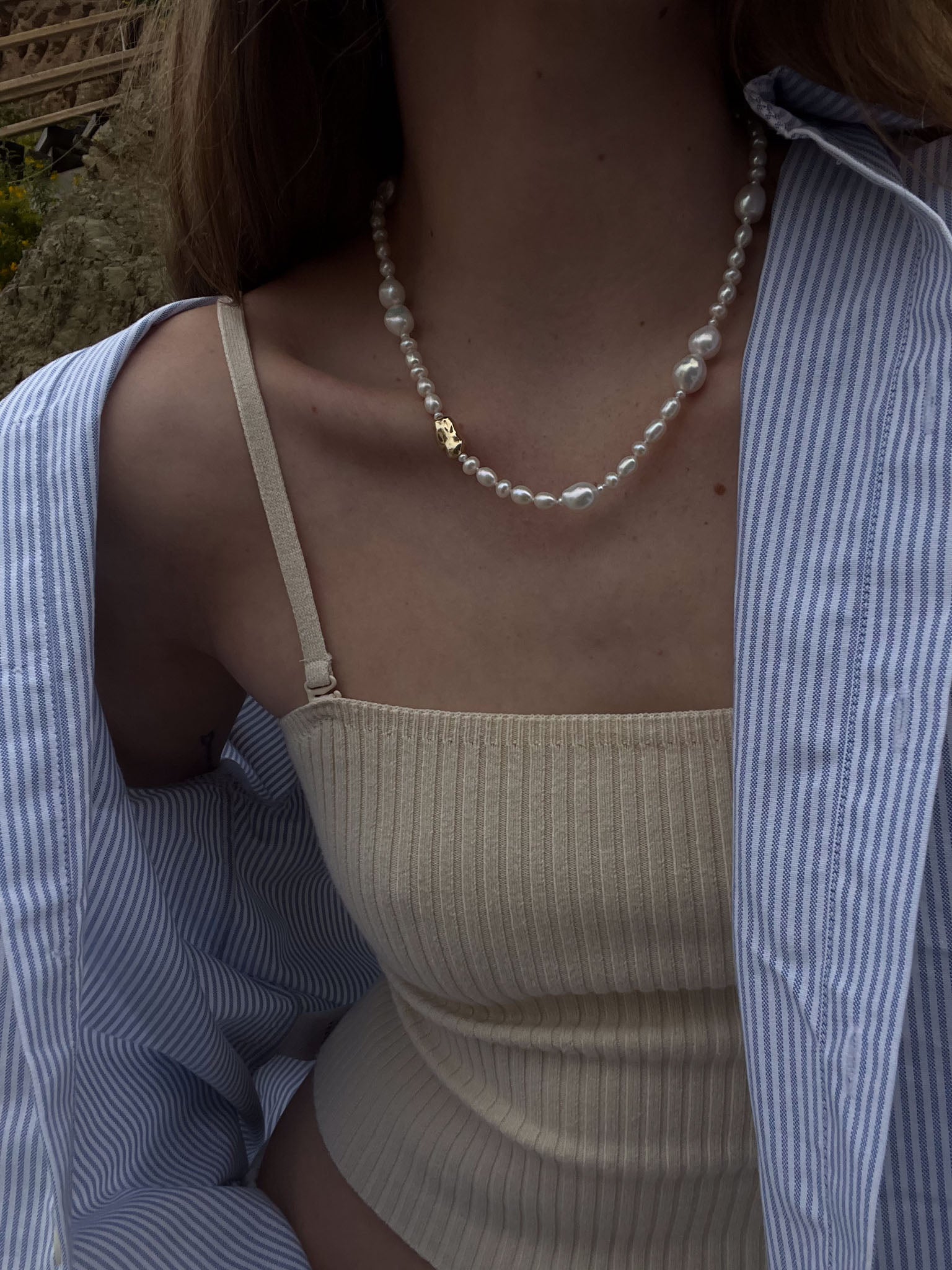 A woman in a stripe top wearing a Kinn Studio 14k Gold Lucy Baroque Pearl Necklace