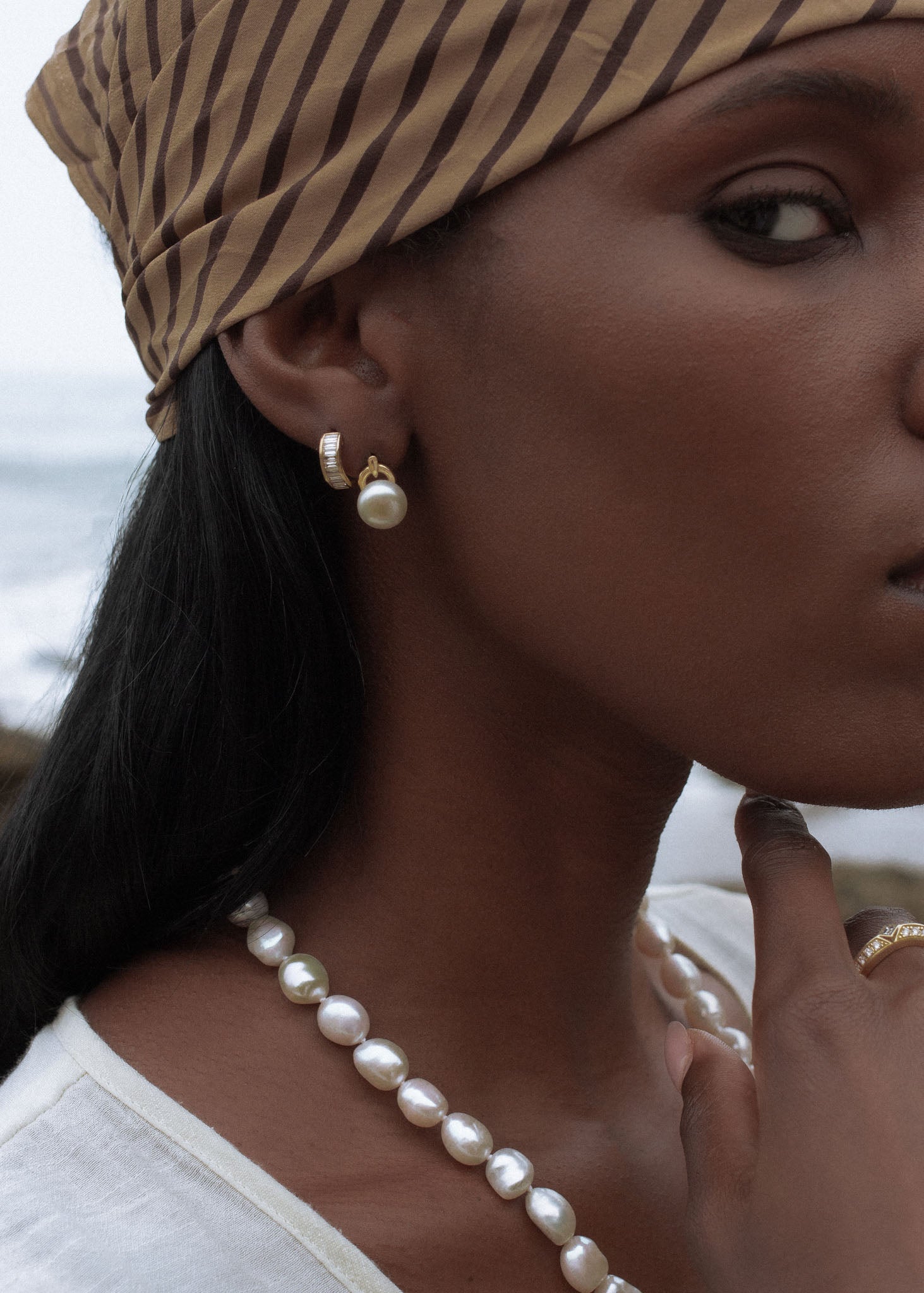 side profile of a woman wearing a Kinn 14k Gold Bobbi Baguette Diamond Huggie Earring in her second piercing layered with a Rose Pearl Stud Earring