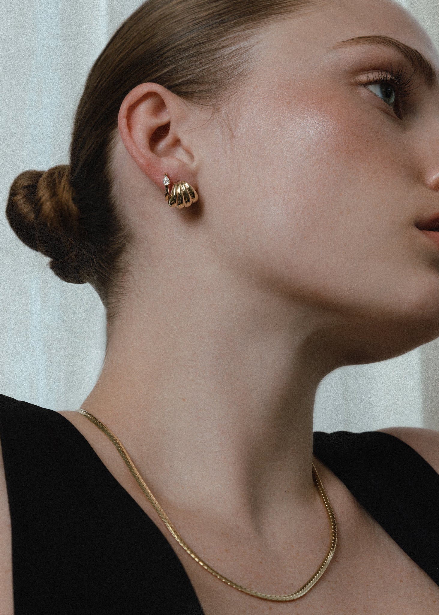 a woman with her hair pulled up in a bun wearing a Kinn 14k Gold Gaia Scallop Earring layered with a diamond hoop