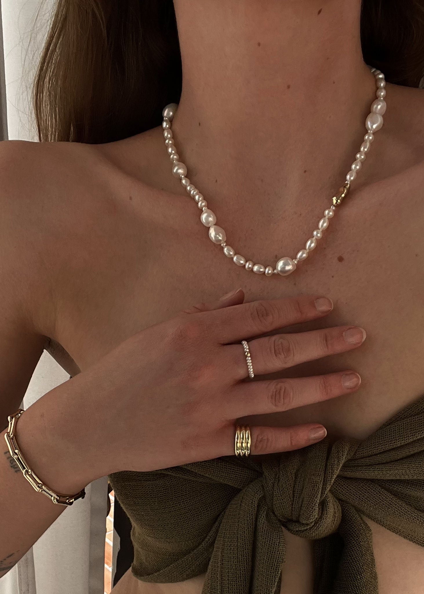 woman in a olive top wearing a Kinn 14k Gold Lucy Baroque Pearl Necklace layered with a Biwa Pearl Ring and Francoise Ring