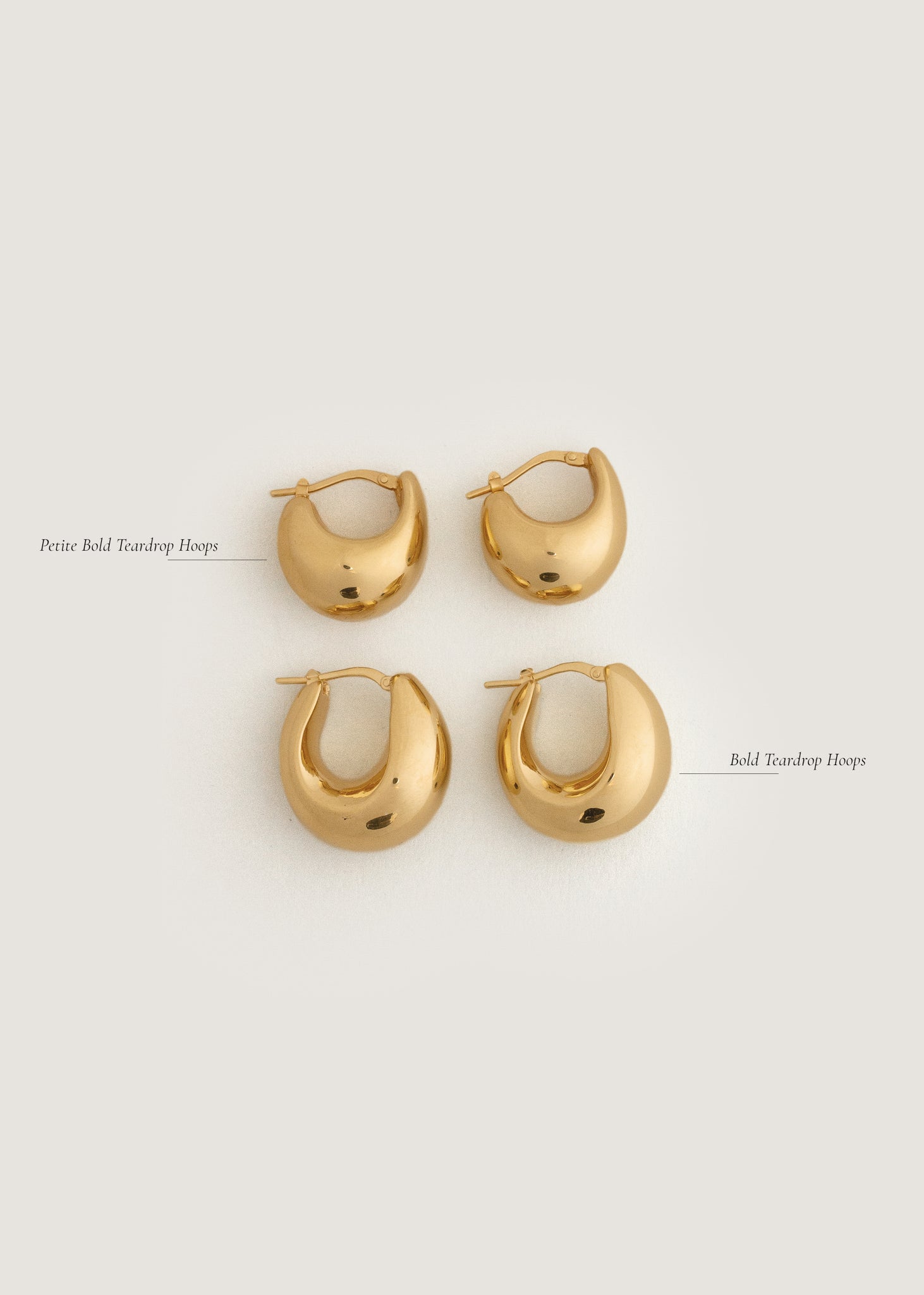Kinn 14k Gold Bold Teardrop Hoop Earrings and 14k Gold Petite Bold Teardrop Hoops laying flat against a white background to show size comparison