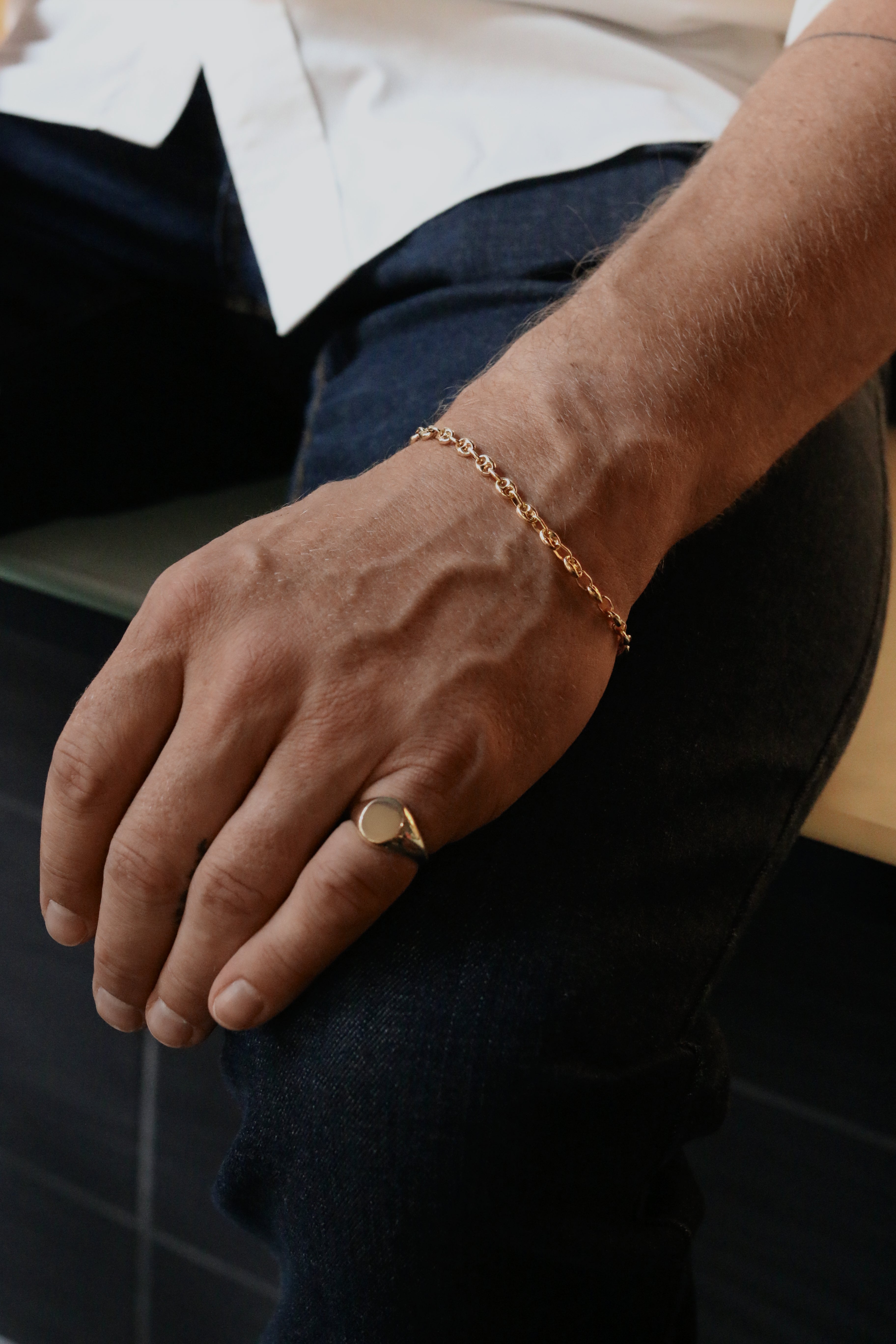 man with hand resting on his leg wearing a Kinn 14k Gold Men's Petite Puffed Mariner Chain Bracelet and a Bold Signet Ring