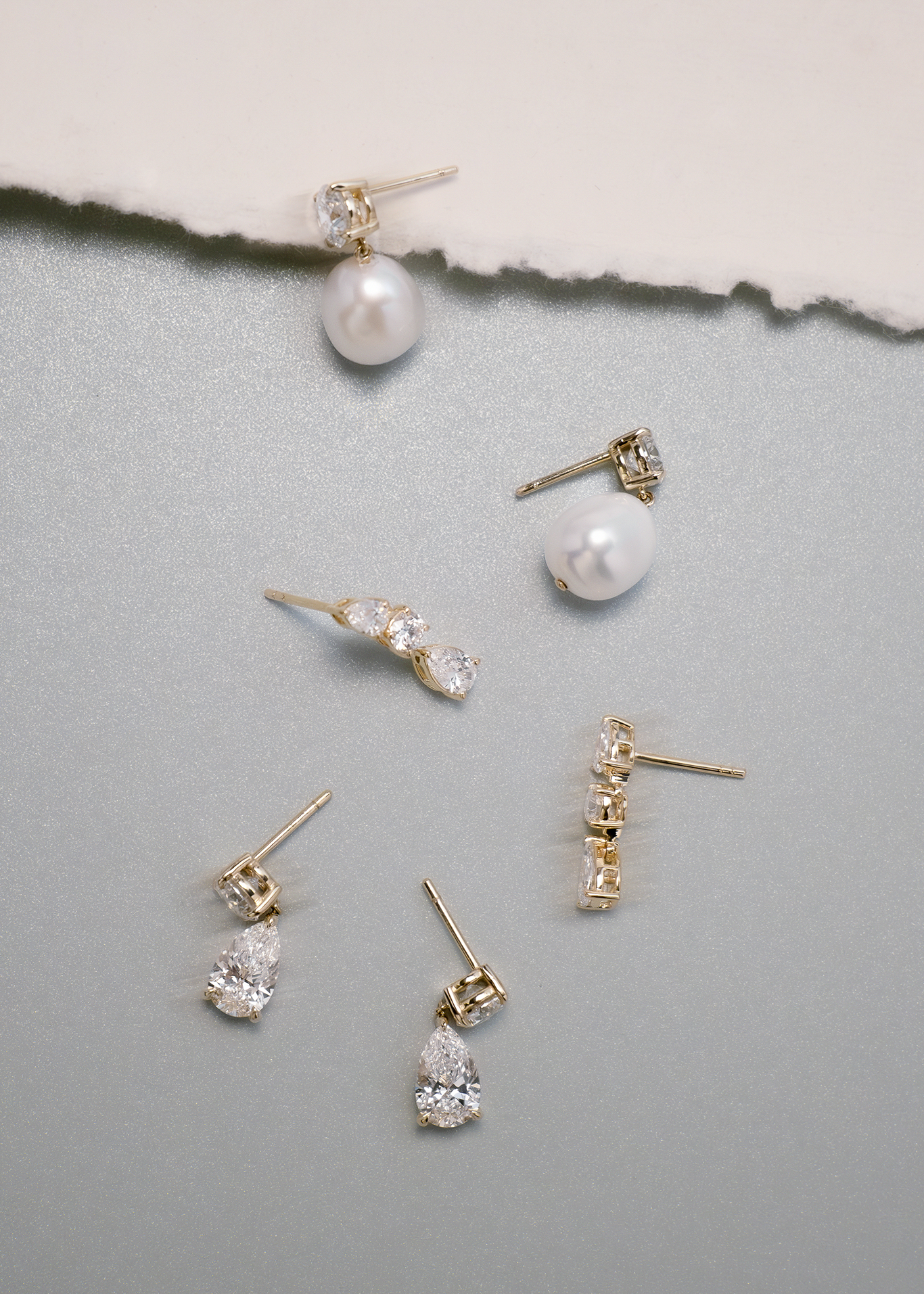 A pair of Kinn Studio 14k Gold Delanie Diamond Baroque Pearl Earrings laying flat alongisde a pair of Third Time's a Charm and Frankie Pear and Round Diamond Earrings