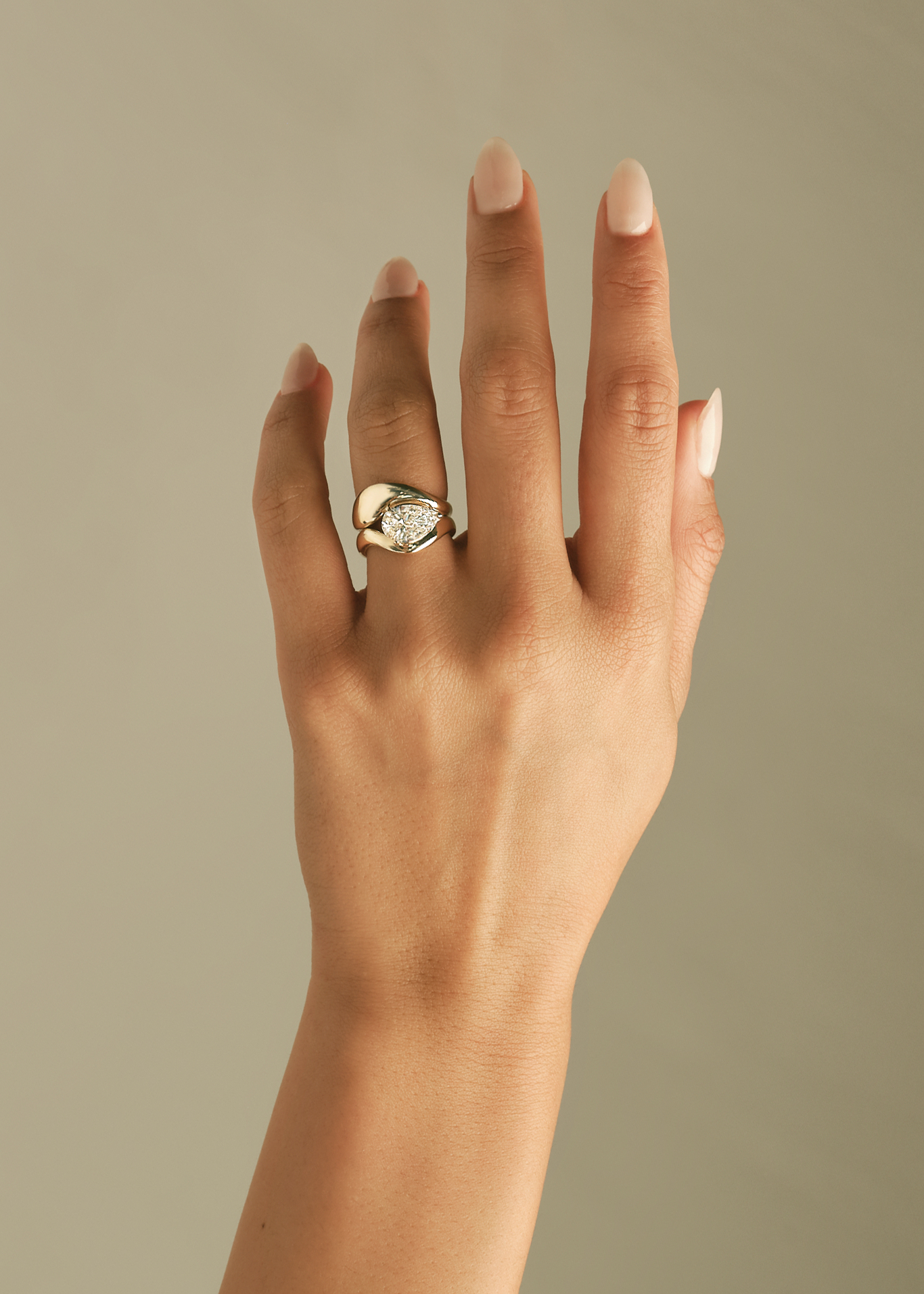 close up of a woman's hand wearing a Kinn 14k Gold Bold Rosewood Curved Stacking Ring stacked on a Solei Pear Diamond Engagement Ring on her left ring finger