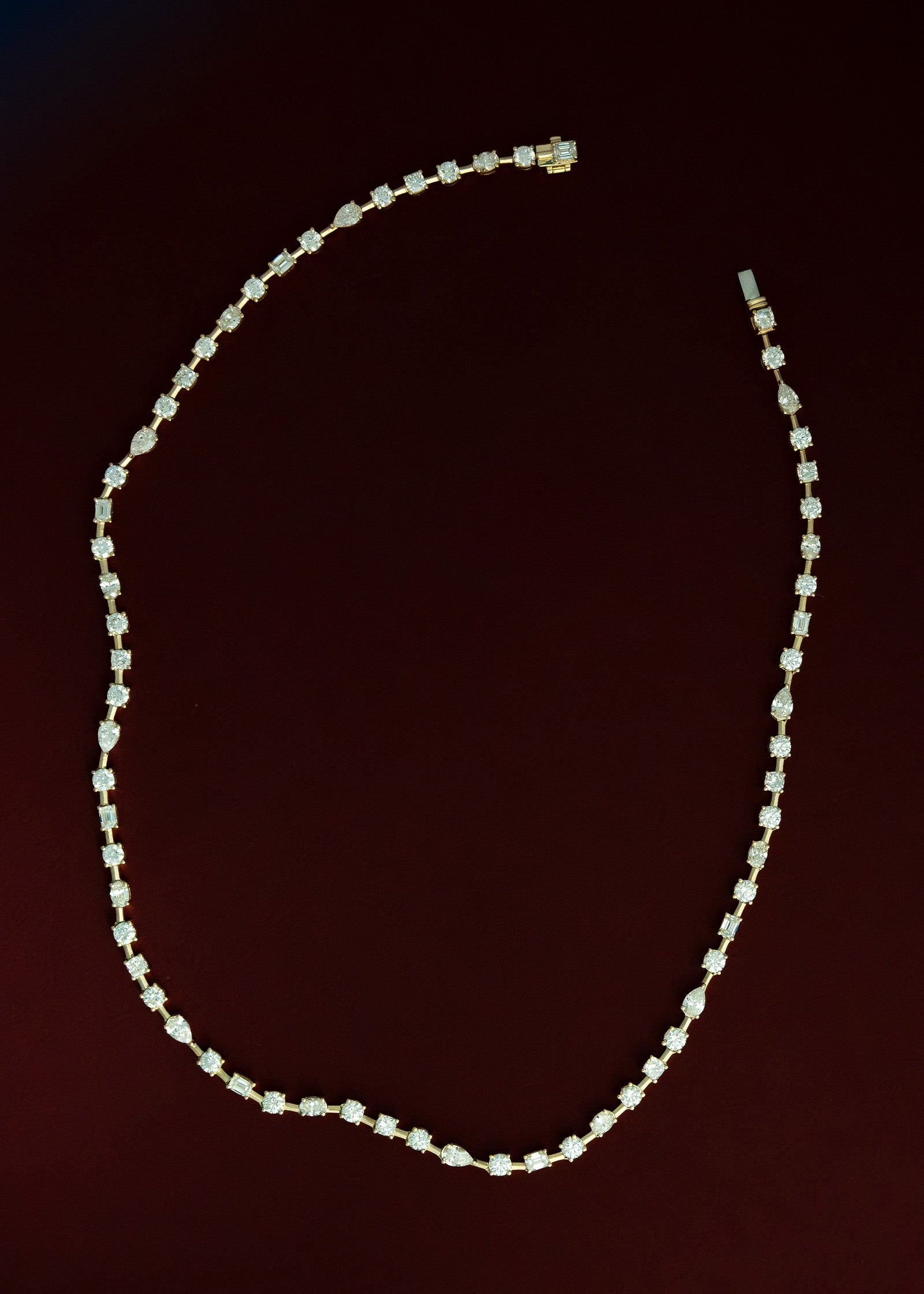 Kinn 14k Yellow Gold Amara Fancy Shape Diamond Tennis Necklace laying flat against a burgundy red background