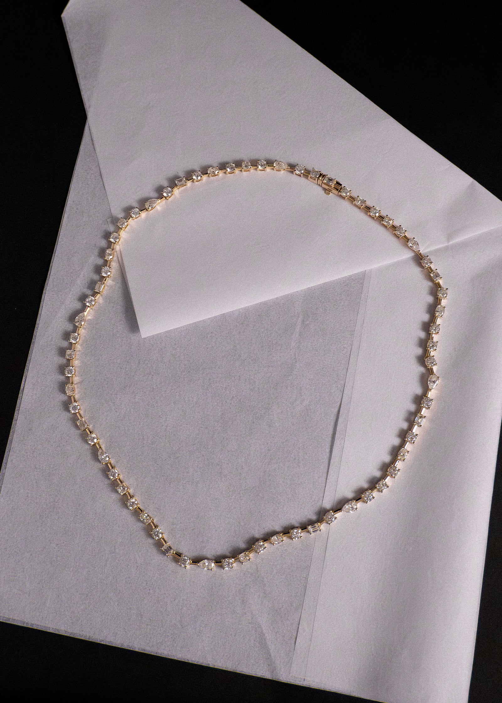 Kinn 14k Yellow Gold Amara Fancy Shape Diamond Tennis Necklace laying on a piece of folded tissue paper