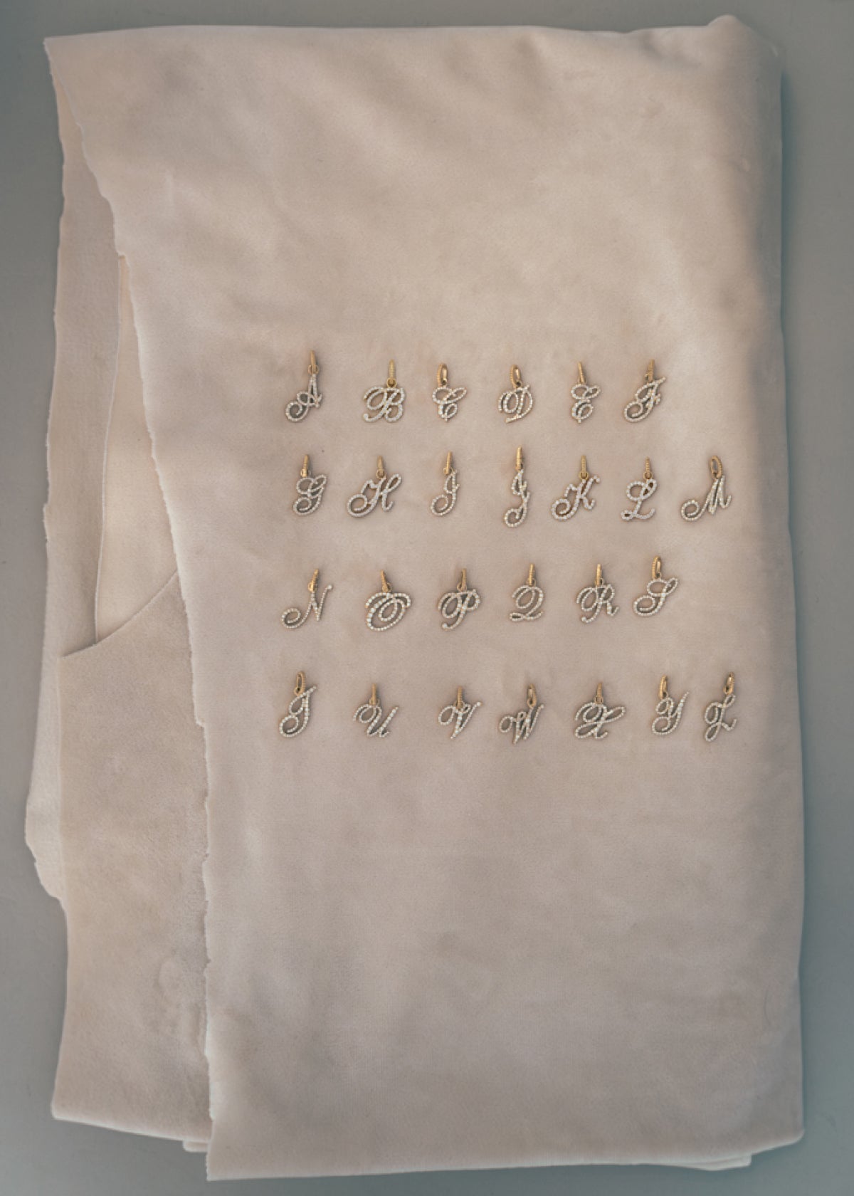 All letter options for the Kinn 14k Gold Pave Diamond Love Letter Pendant laid out on a piece of folded fabric
