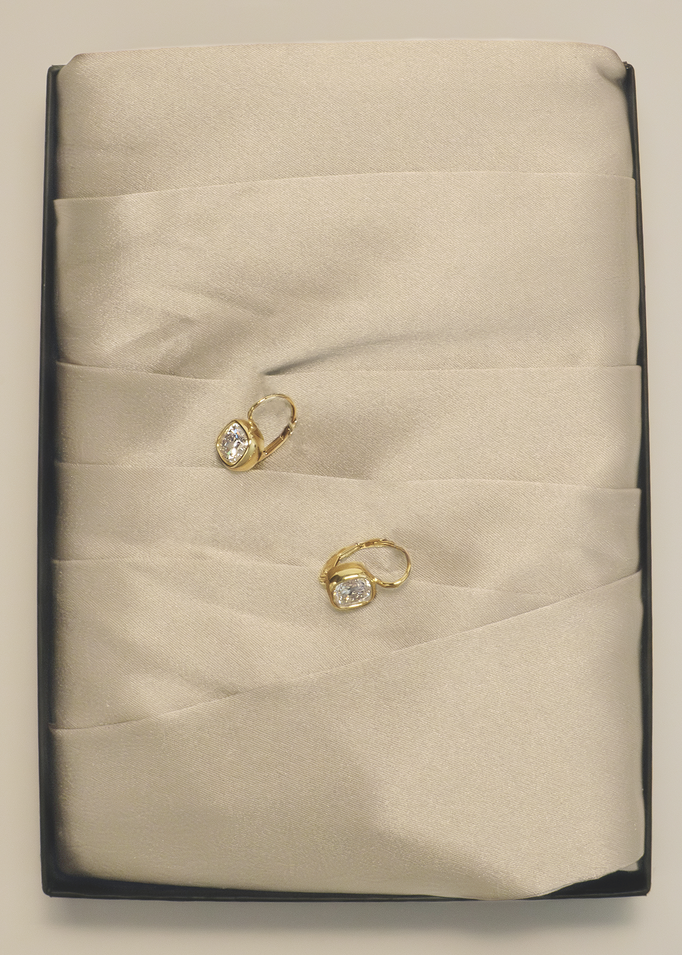 A pair of Kinn 14k Gold Harper 2ctw Cushion Cut Diamond Drop Earrings nested between folds of cream satin fabric