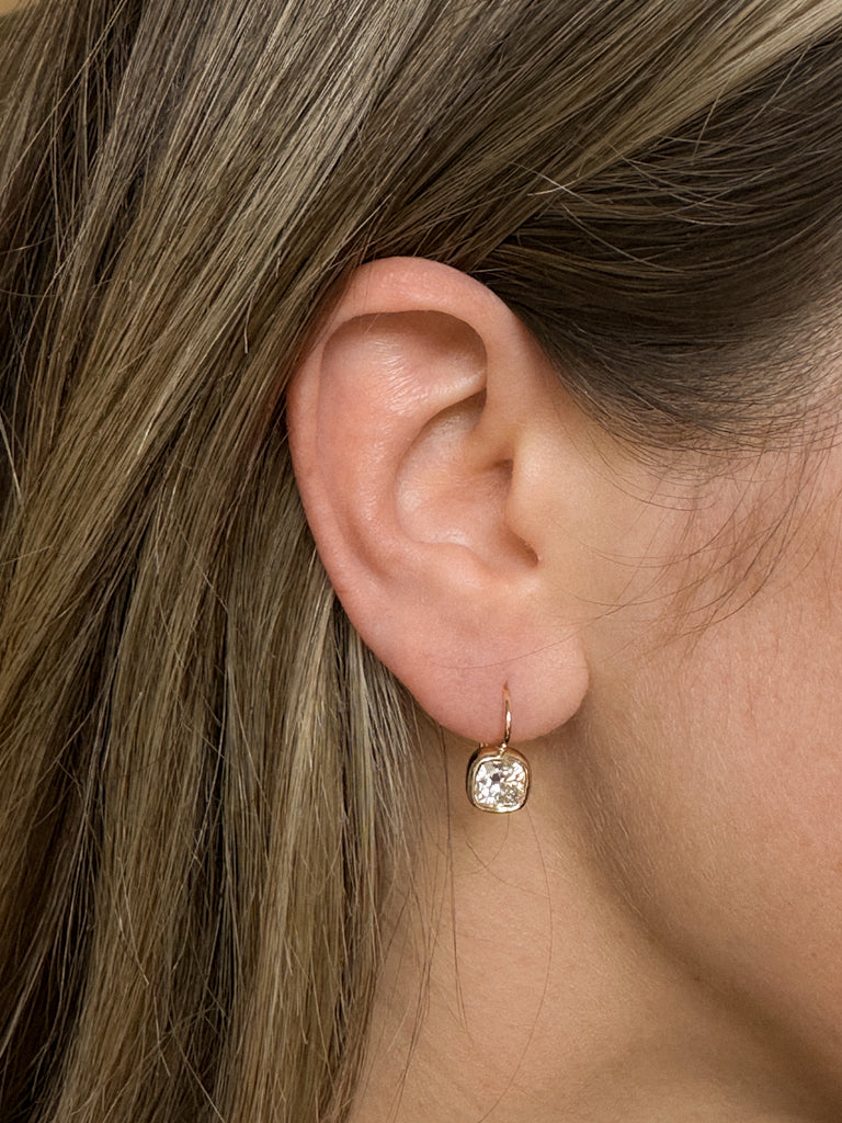 A close up of a woman wearing a Kinn 14k Gold Harper 2ctw Cushion Cut Diamond Drop Earrings