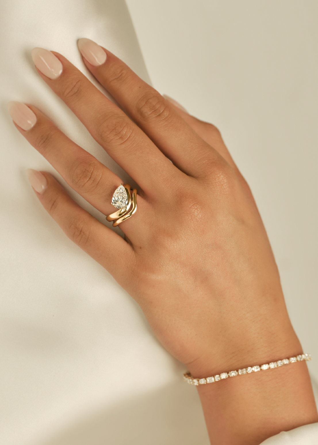 a close up of a woman's hand wearing a Kinn 14k Gold Rosewood Curved Stacking Band Ring stacked under a 14k Gold Kira Pear Diamond Engagement Ring