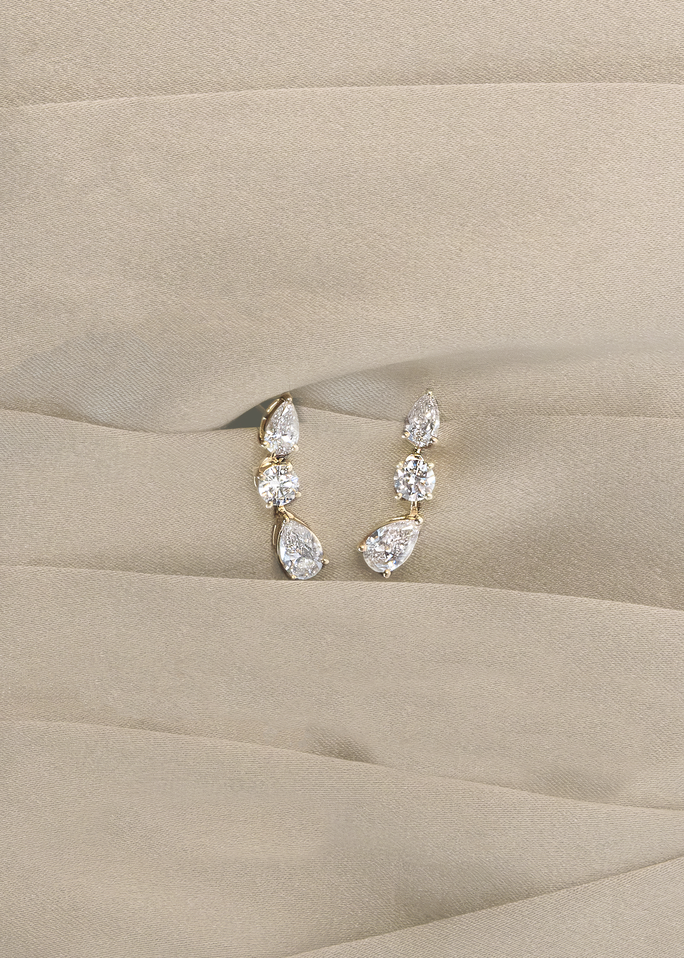 Kinn 14k Gold Third Time's a Charm Drop Earrings Pear 2.7ctw Diamond laying against a cream fabric background