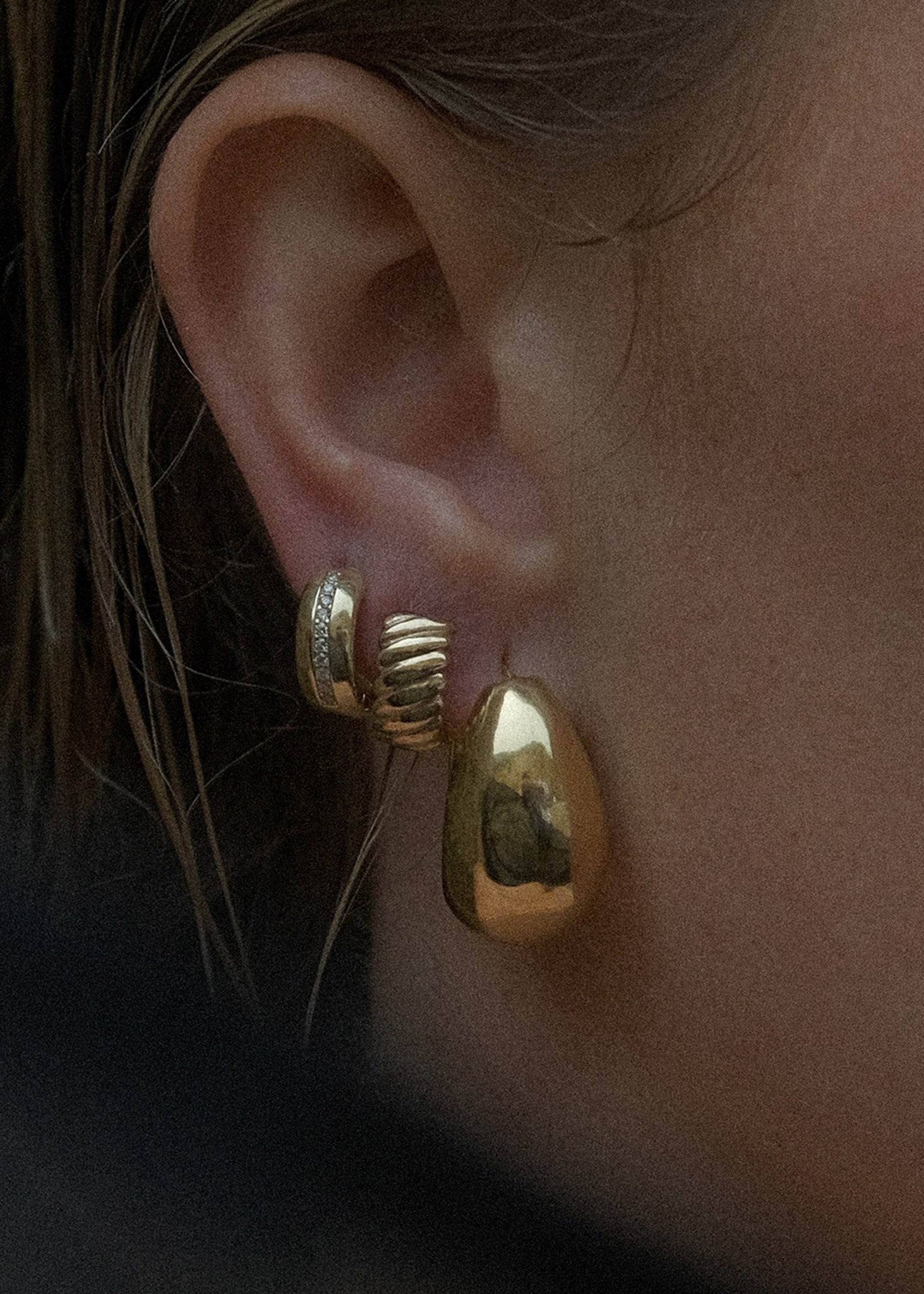 close up woman's ear wearing a Kinn 14k Gold Bold Teardrop Hoop Earring layered with two other diamond and gold huggies