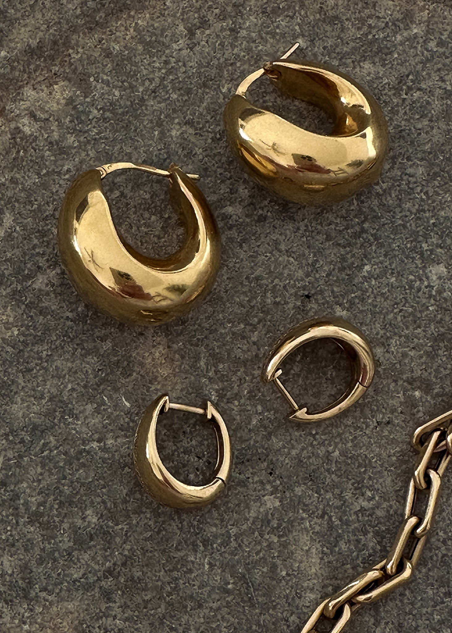 A pair of Kinn 14k Gold Bold Teardrop Hoop Earrings laying next to a pair of petite teardrop hoop earrings